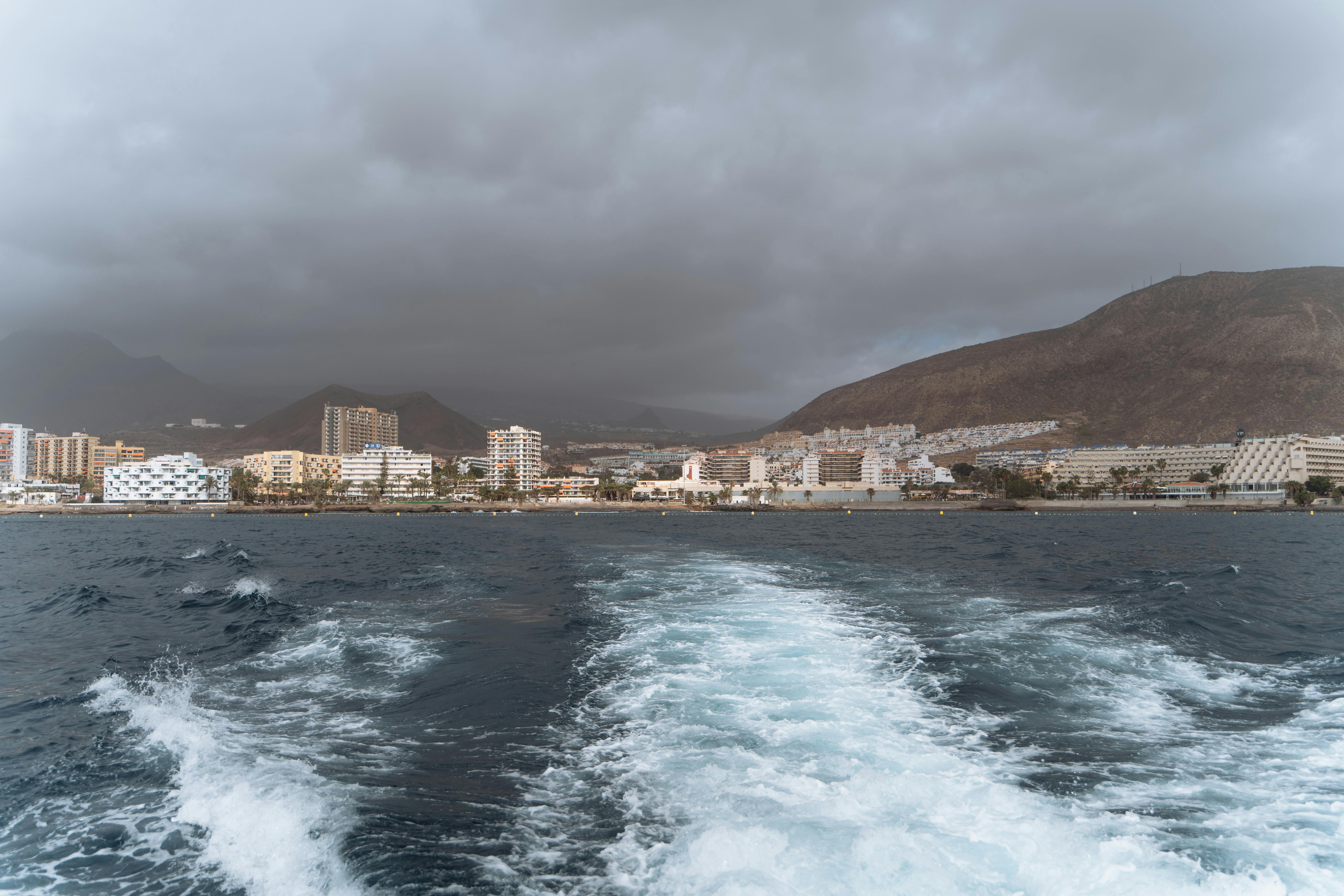 Dramatic view of a Canary Islands coastal city with looming clouds over modern buildings and ocean.