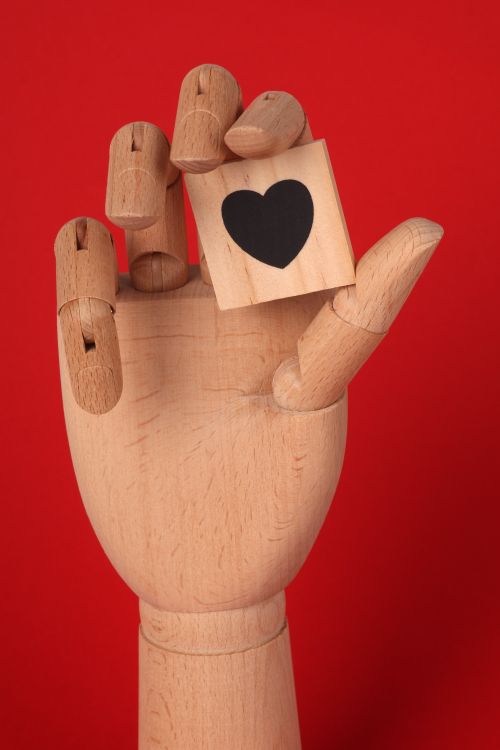 Free A wooden mannequin hand holds a heart block against a bold red backdrop. Stock Photo