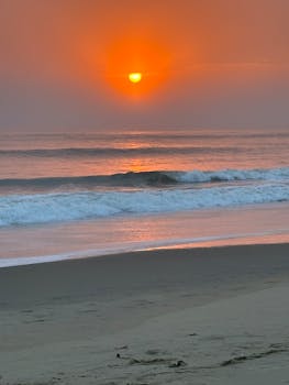 A stunning sunrise over a tranquil beach with gentle waves and a vibrant sky.