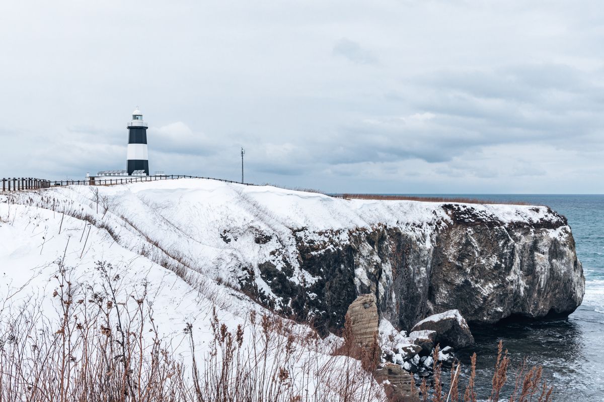 Winter lighthouse on snowy cliffs in Hokkaido — dramatic Pacific coastline