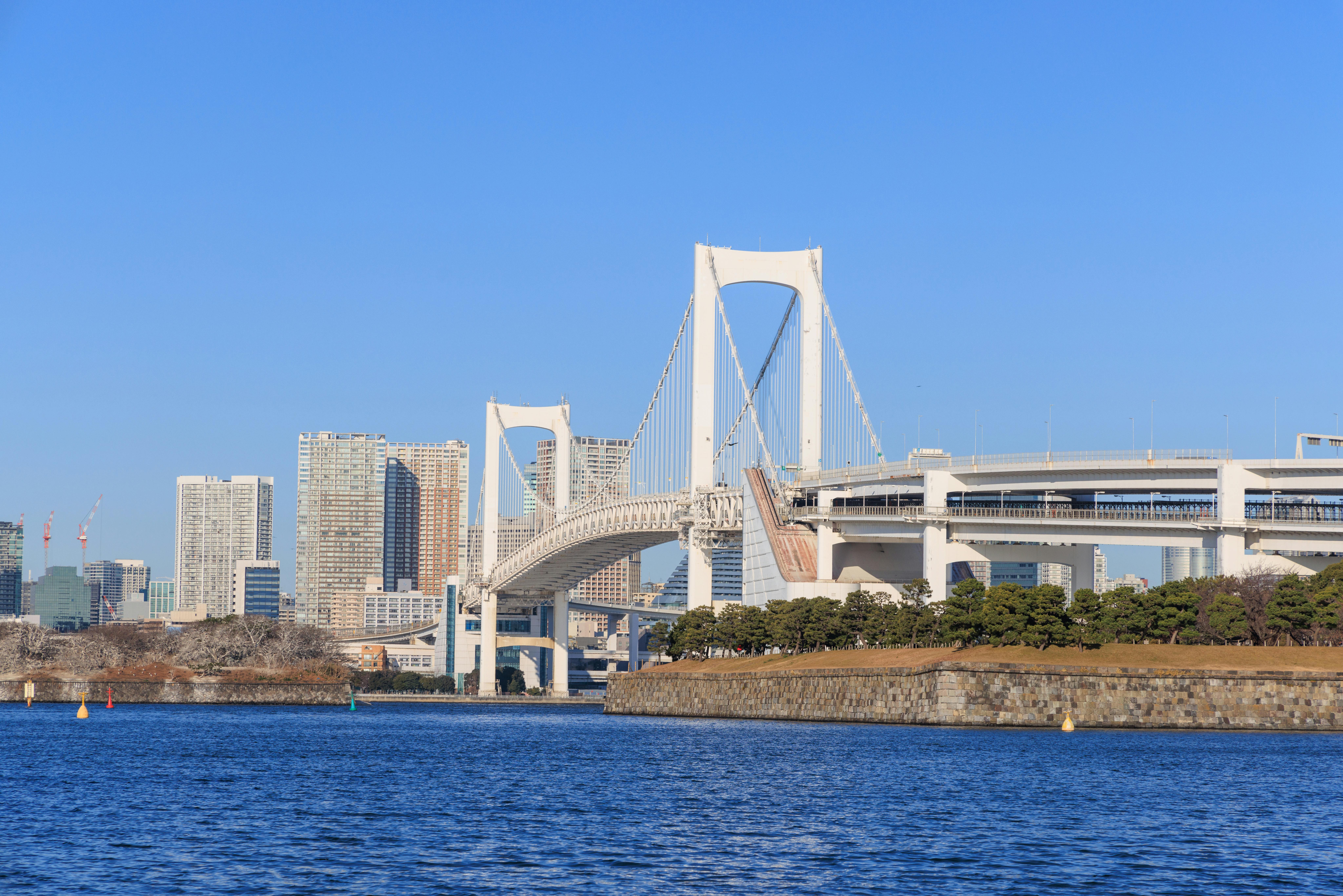 Rainbow Bridge in Tokyo Bay at twilight with the bridge lit in rainbow colors reflecting on water and Tokyo skyline behind