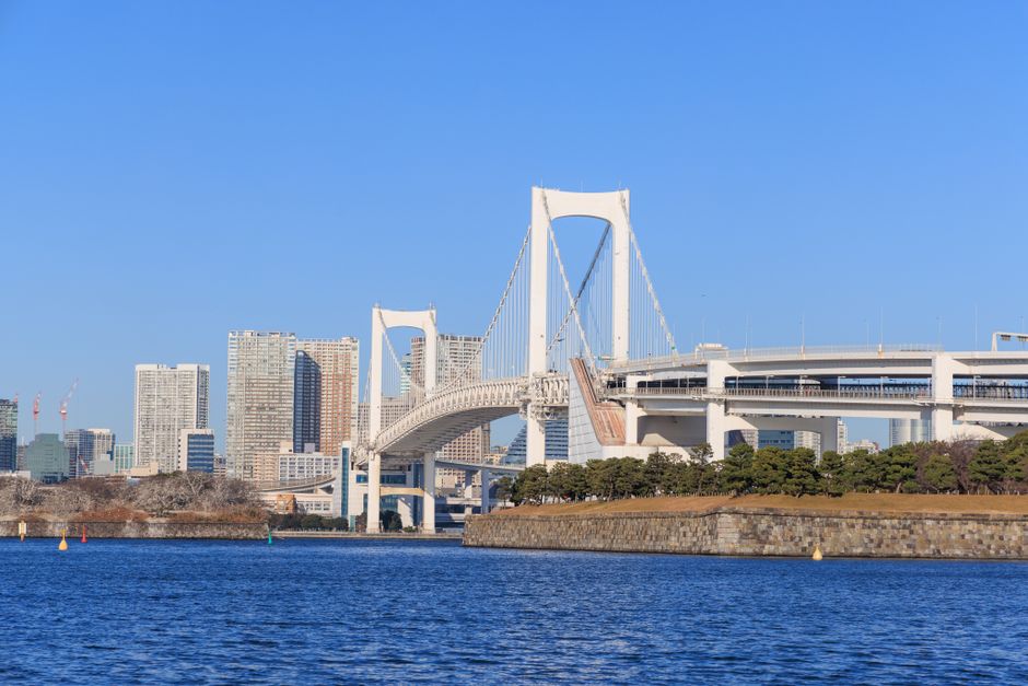 View of the Rainbow Bridge and Tokyo skyline on a bright day, highlighting architectural beauty.