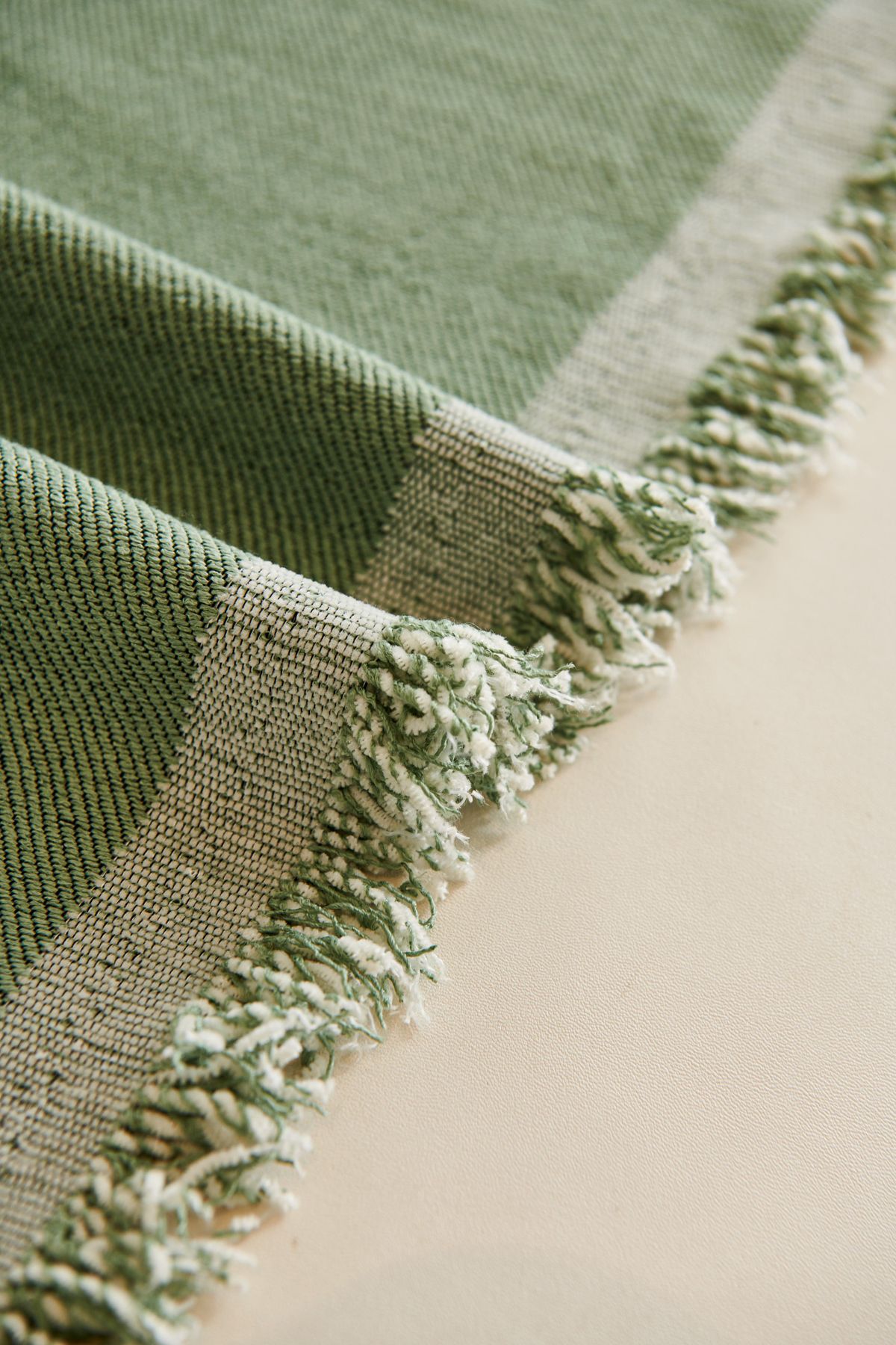Close-up of green woven fabric and fringe, showing surface structure as well as color.