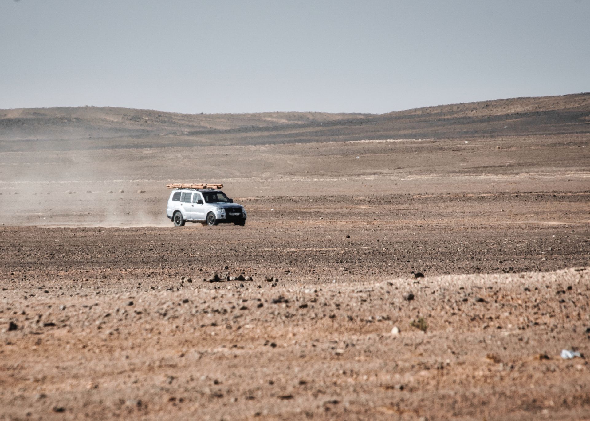 An off-road vehicle travels through the vast, arid Sahara Desert landscape in Morocco.