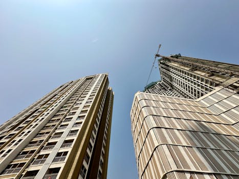 Upward view of modern skyscrapers and construction crane in Mumbai against a clear blue sky.