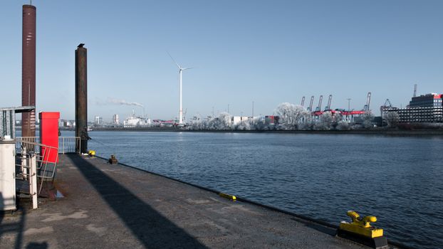 Frosty winter scene of Hamburg harbor with a wind turbine and industrial skyline.