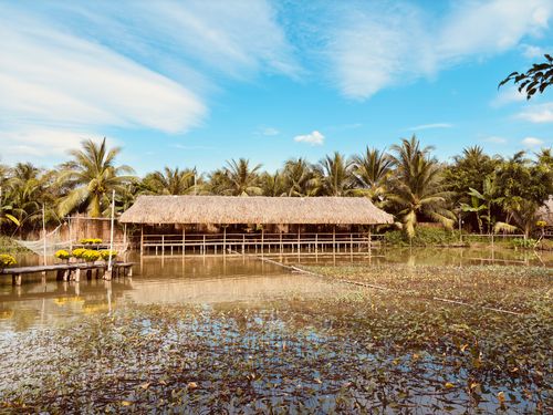 Free Serene bamboo hut surrounded by palm trees and reflective water in tropical landscape. Stock Photo