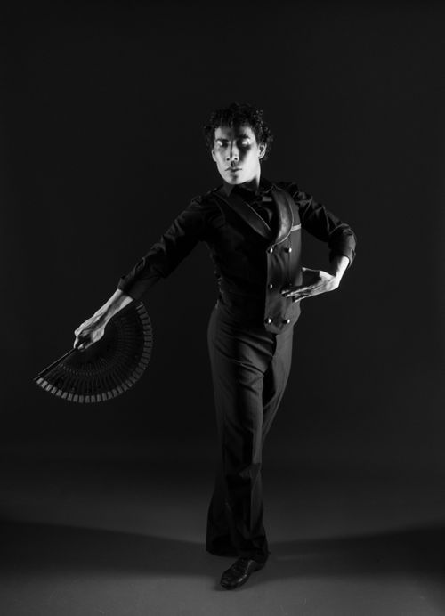 Free Elegant male dancer striking a pose with a fan against a dark background. Stock Photo