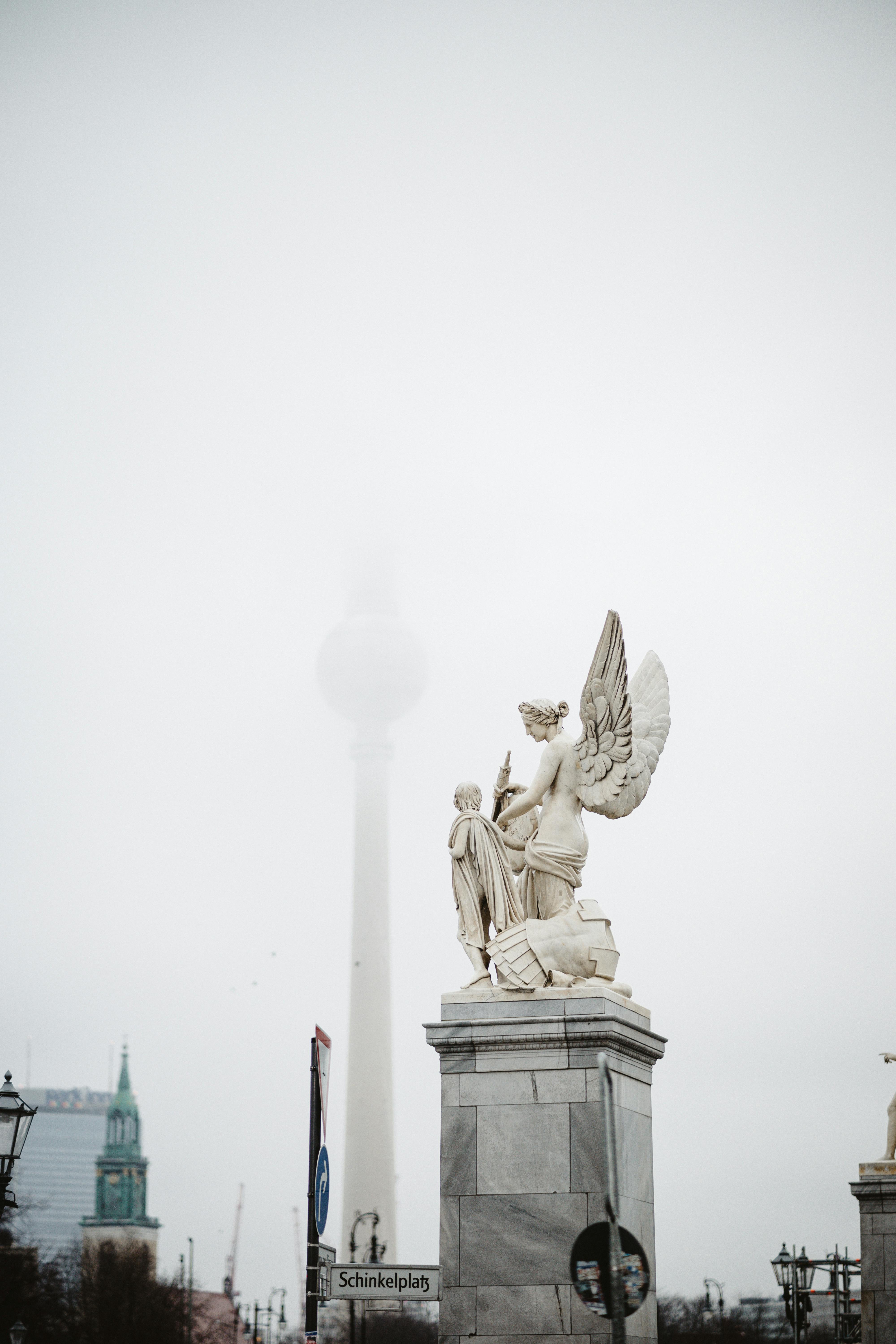 Statue of angel and figure in Berlin with TV Tower backdrop on a foggy day.