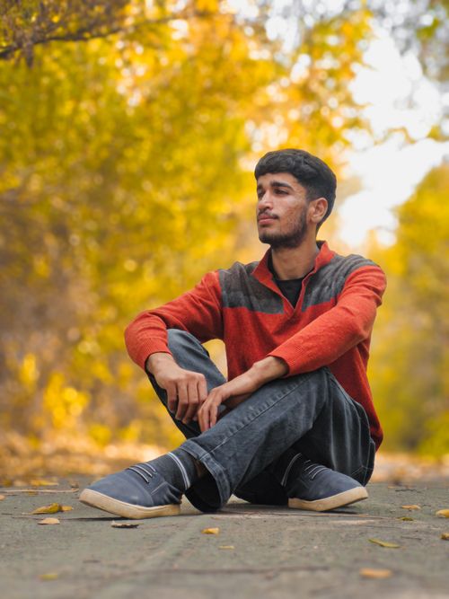 Free A young man seated on a path in a vibrant autumn forest setting. Stock Photo