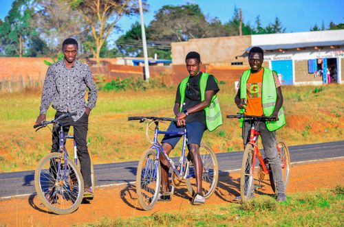 Free Three men pose with bicycles on a sunny rural road, wearing casual and reflective attire. Stock Photo