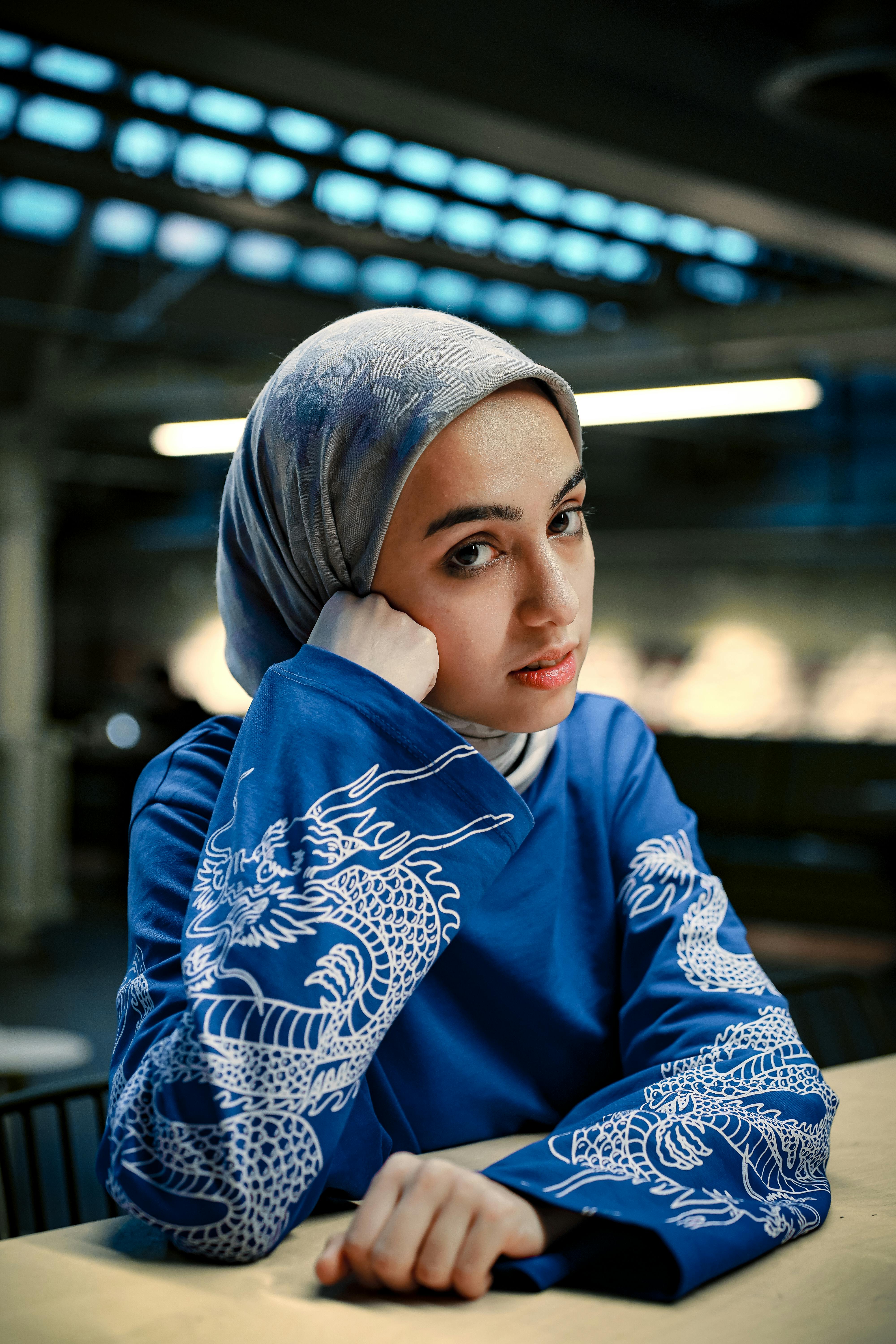 Woman wearing a blue hoodie with dragon design indoors, looking thoughtful.