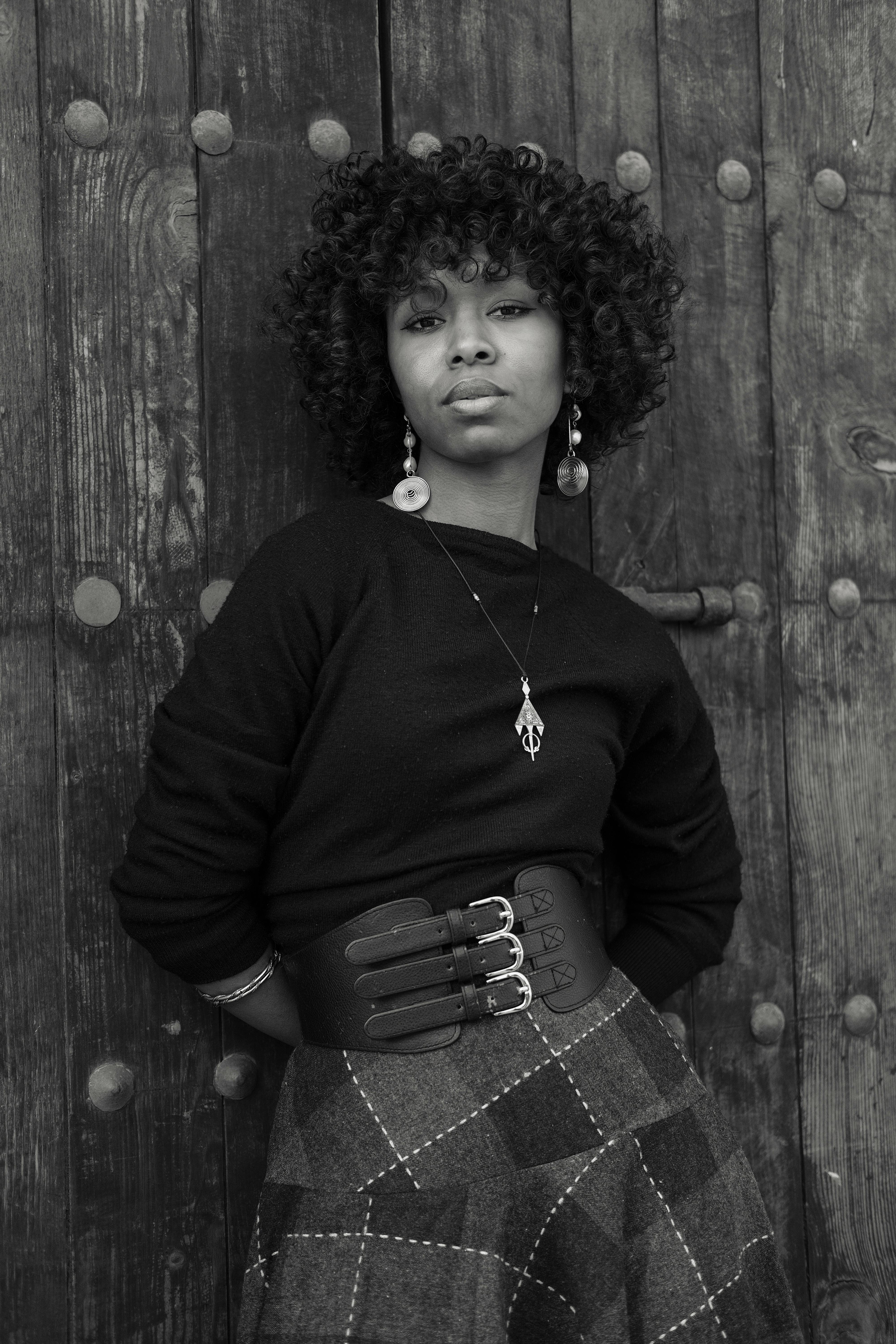 Elegant black and white portrait of a woman leaning against a wooden door in Rabat, Morocco.