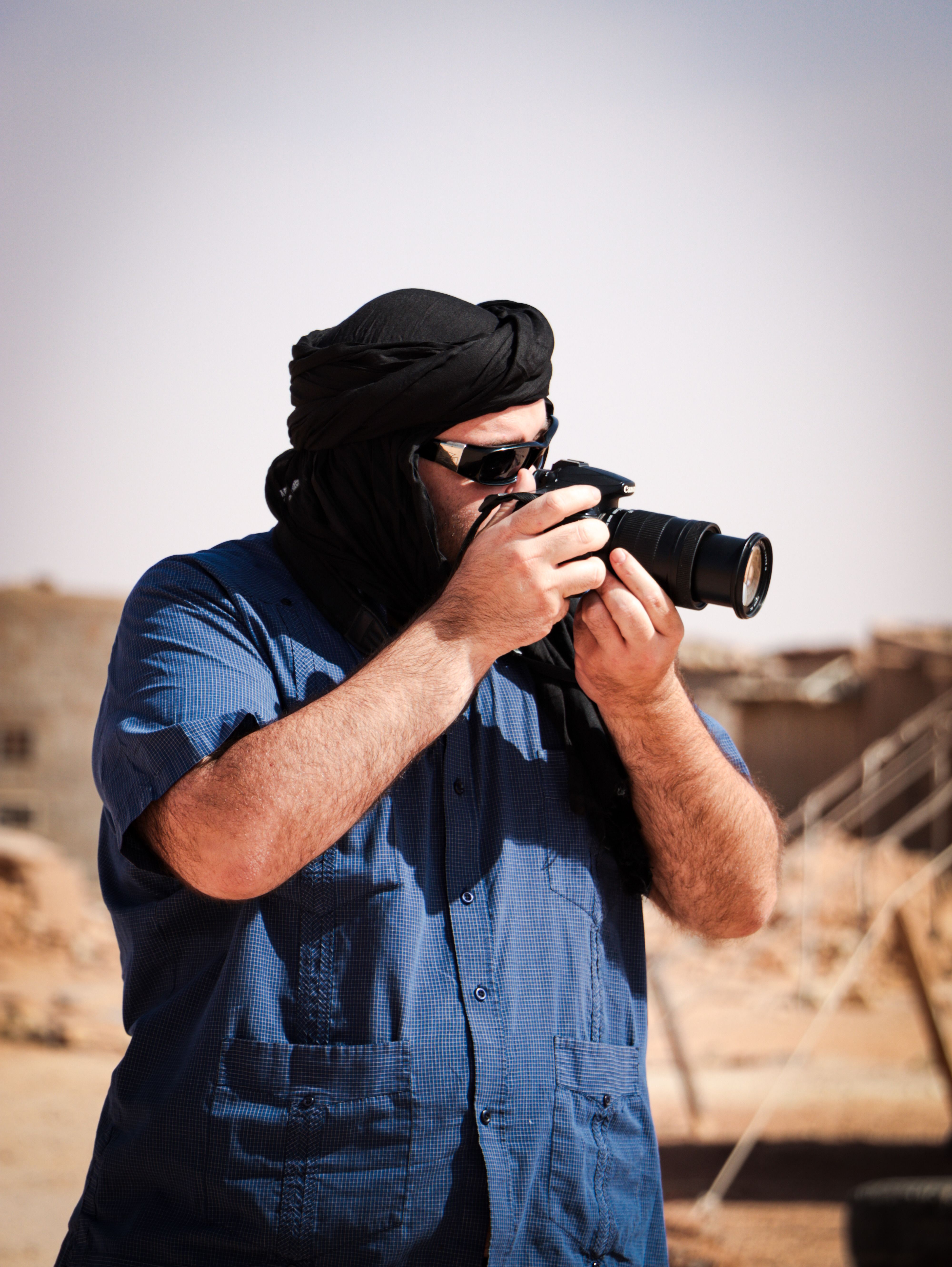A photographer wearing traditional attire capturing the desert scenery in Tindouf, Algeria.