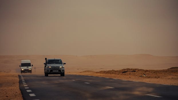 Vehicles traveling on an empty desert road with a dramatic sandy landscape.