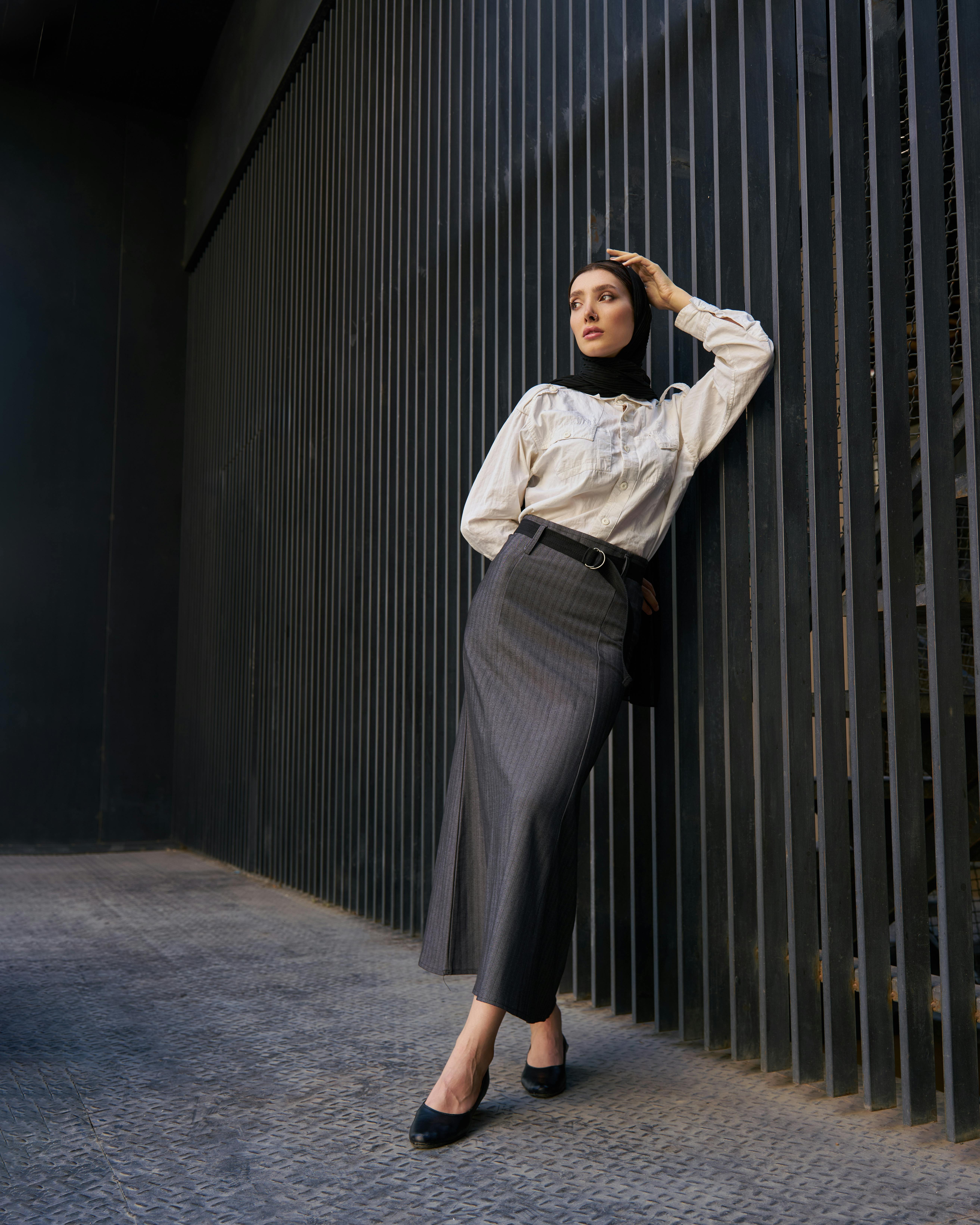 Stylish woman in a hijab standing against a modern, textured wall in urban setting.