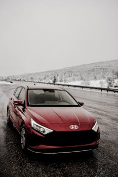 A red sedan parked on a wet mountain road in winter snowy conditions, showcasing vehicle design.