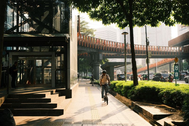 A man rides his bicycle through a bustling, sunlit street in Jakarta, Indonesia.