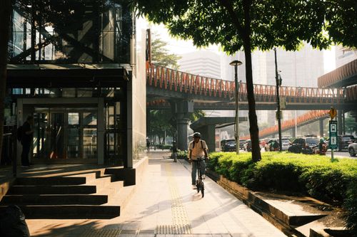 Free A man rides his bicycle through a bustling, sunlit street in Jakarta, Indonesia. Stock Photo