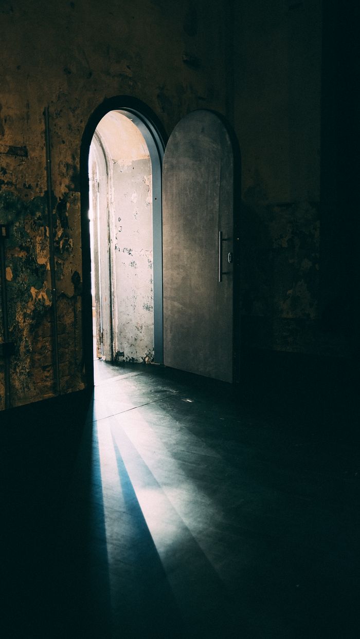 Daylight falling through a tall arched door into a dark room, by Sami TÜRK on Pexels