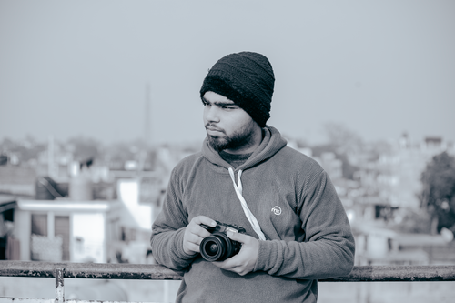 Free Young man holding a camera on a rooftop with a city background in India. Stock Photo