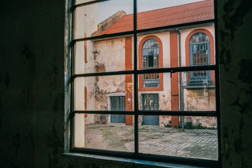 Free View of a weathered red brick building's courtyard through a vintage window. Stock Photo
