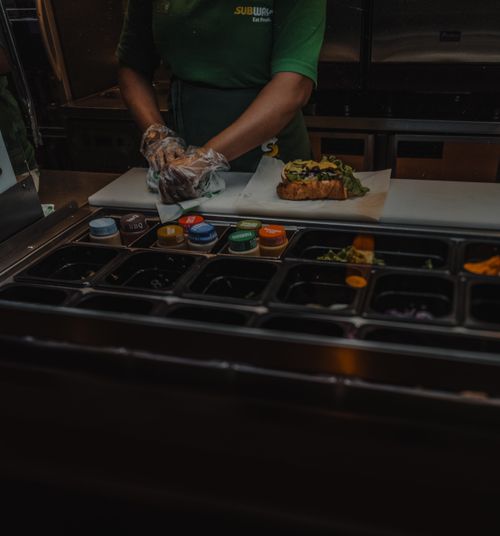 Free A Subway employee prepares a fresh sandwich with various ingredients at a fast-food restaurant. Stock Photo