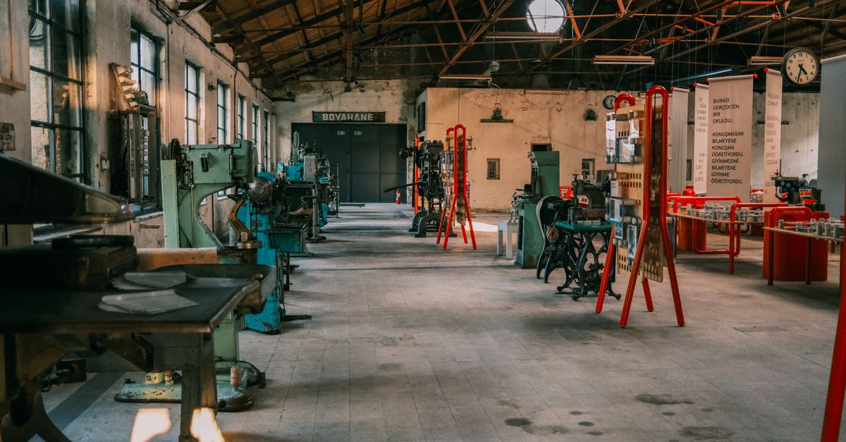 An expansive industrial workshop featuring vintage machinery and tools under a wooden roof.