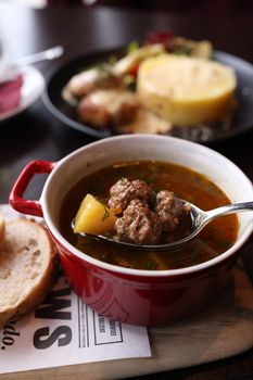 Delicious meatball soup with potatoes served in a red ceramic bowl with bread.