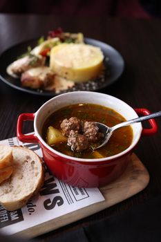 Delicious meatball soup with vegetables and bread on a dark wooden table.