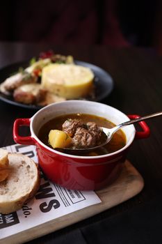 Close-up of delicious meatball soup in a red pot with bread slice.