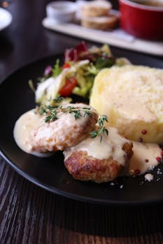Elegant meal featuring mashed potatoes, meat patties, and fresh salad on a black plate.