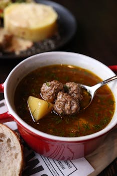 Delicious meatball soup with potatoes and herbs in a red bowl.
