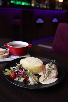 Elegant restaurant chicken plate with salad, mashed potatoes, and soup.