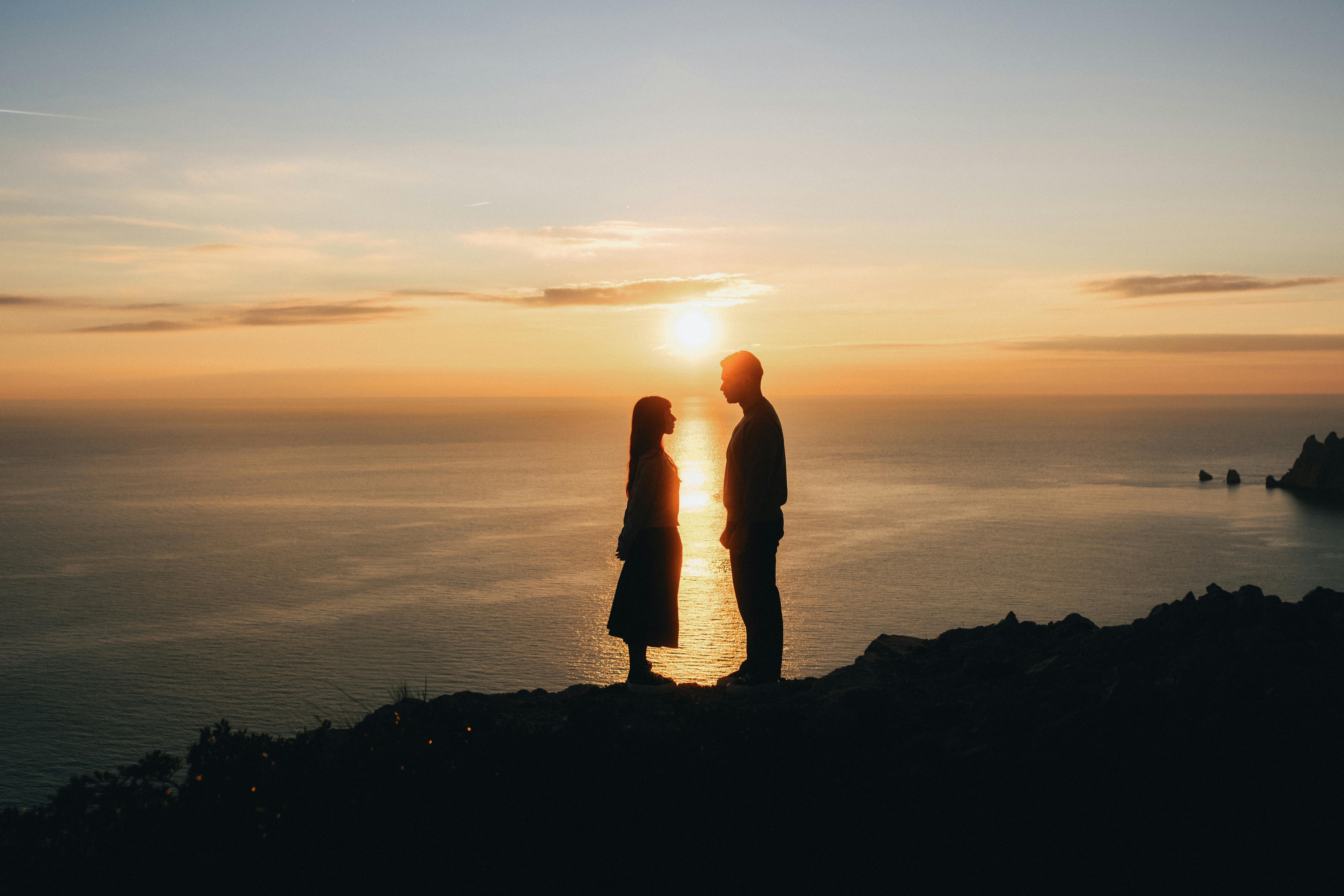 Silhouette of a couple standing on a cliff with a stunning sunset over the sea in Marseille, France.