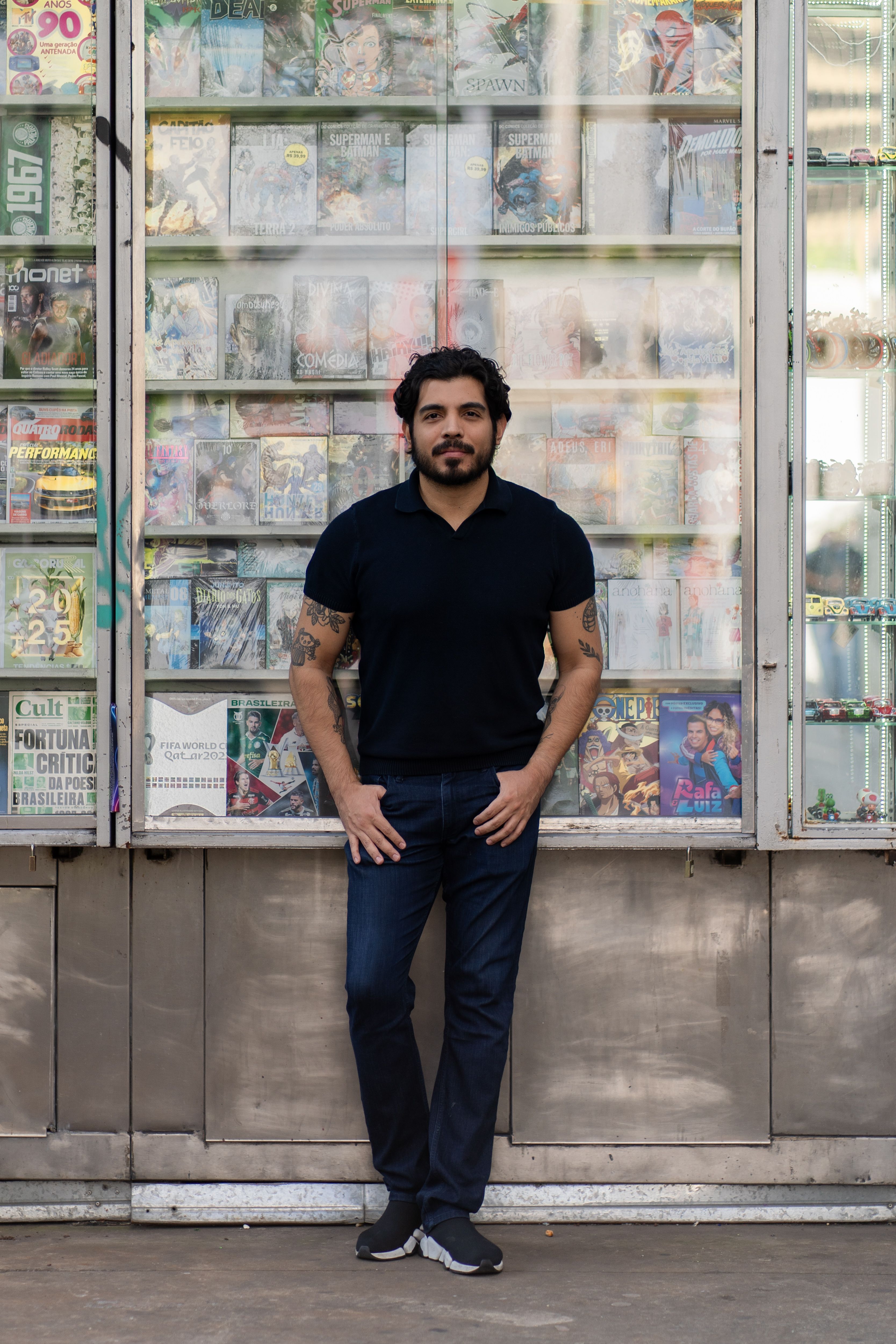 Man standing casually in front of a comic book stand, displaying various titles.