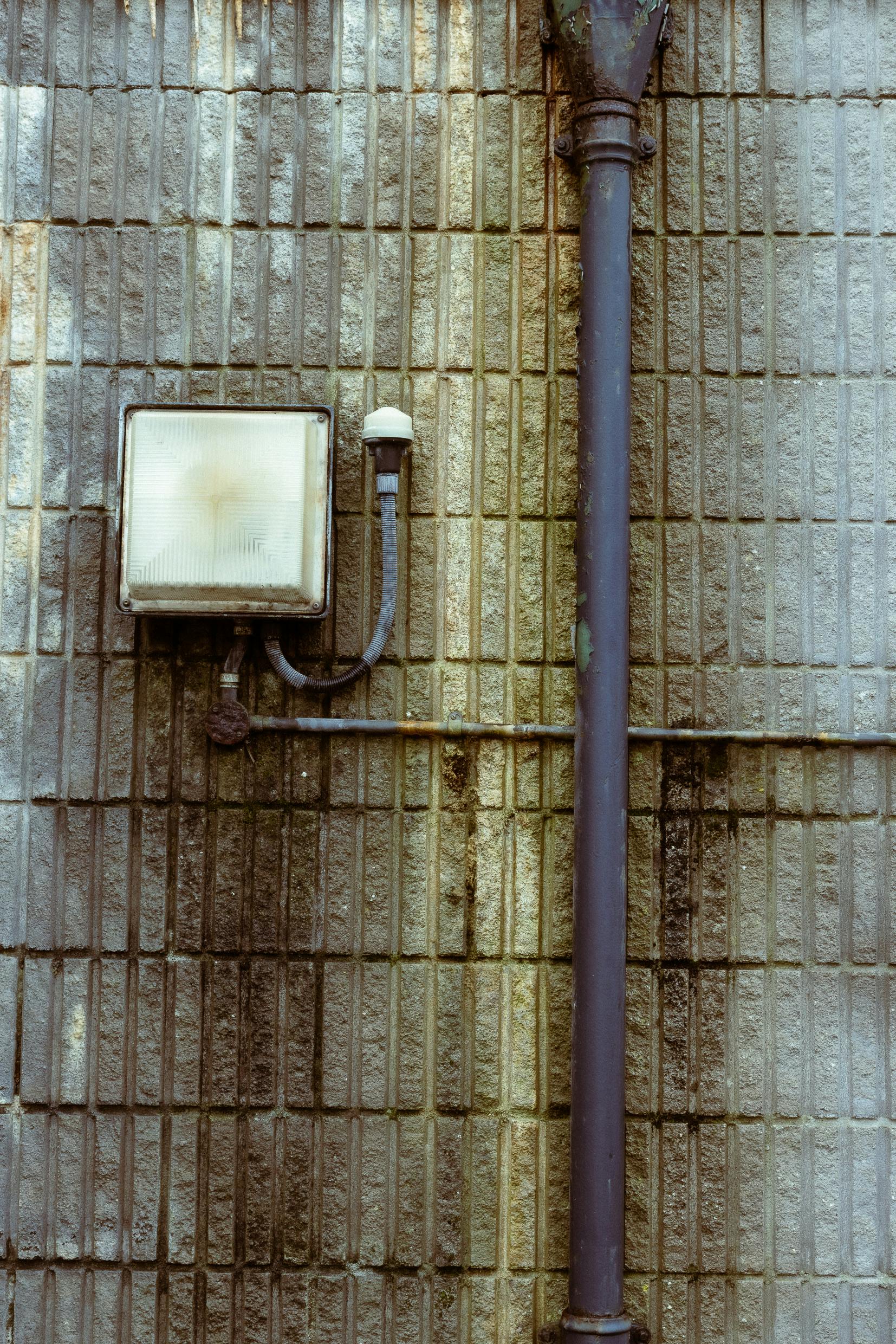 Gratuit Prim-plan al unui zid de cărămidă deteriorat cu iluminat industrial și conducte în Plymouth. Fotografie de stoc