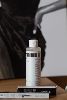 Close-up of a skincare bottle with makeup books on a wooden desk.