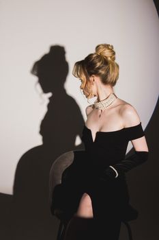 Chic woman in black dress and pearls casting a shadow on a wall, embodying elegance and mystery.