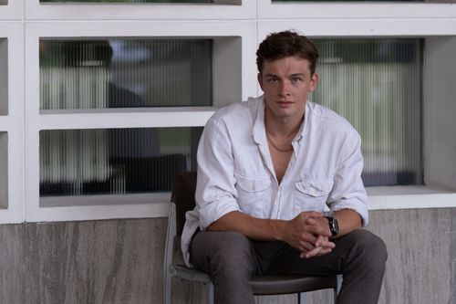 Free Relaxed young man in a white shirt seated indoors against a modern wall. Stock Photo
