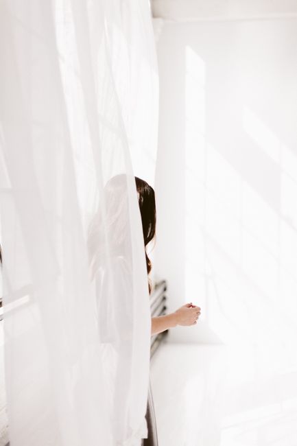 A mysterious silhouette of a woman standing behind sheer curtains with sunlight casting shadows.
