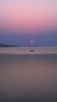 Tranquil pink sunset over a calm lake in Bhopal, India, featuring a solitary boat.