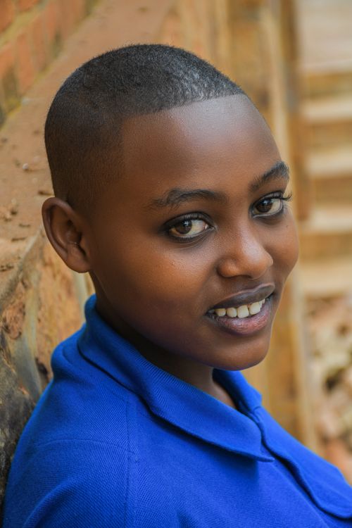 Free Portrait of a smiling young adult in a blue shirt against a rustic brick background. Stock Photo
