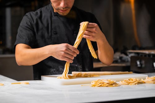 Free A chef skillfully handcrafting fresh pasta in a restaurant kitchen, showcasing culinary artistry. Stock Photo
