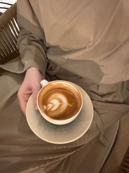 Free A person holding a latte with intricate latte art, dressed in neutral tones. Stock Photo