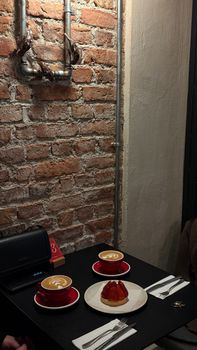 Charming cafe with lattes and dessert on table against rustic brick wall.