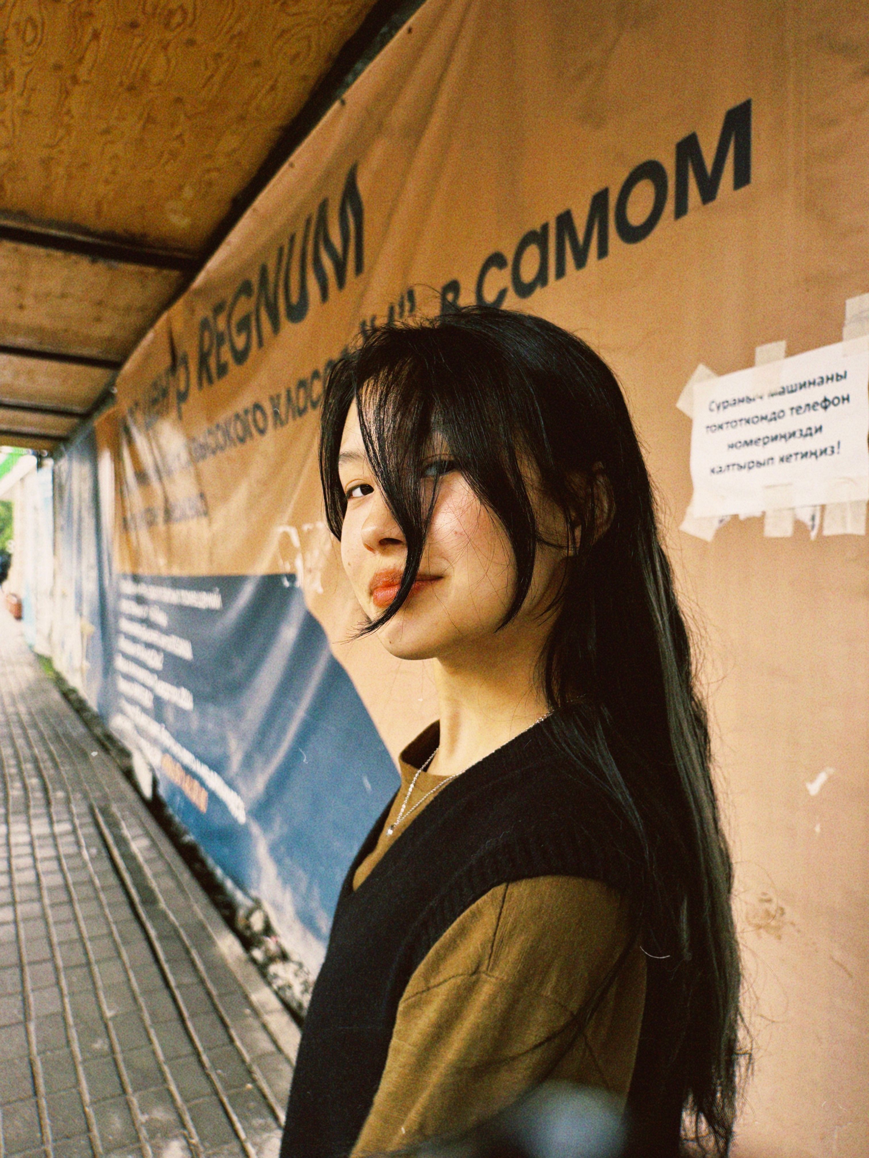 Portrait of a young woman standing on a city sidewalk with urban signage.