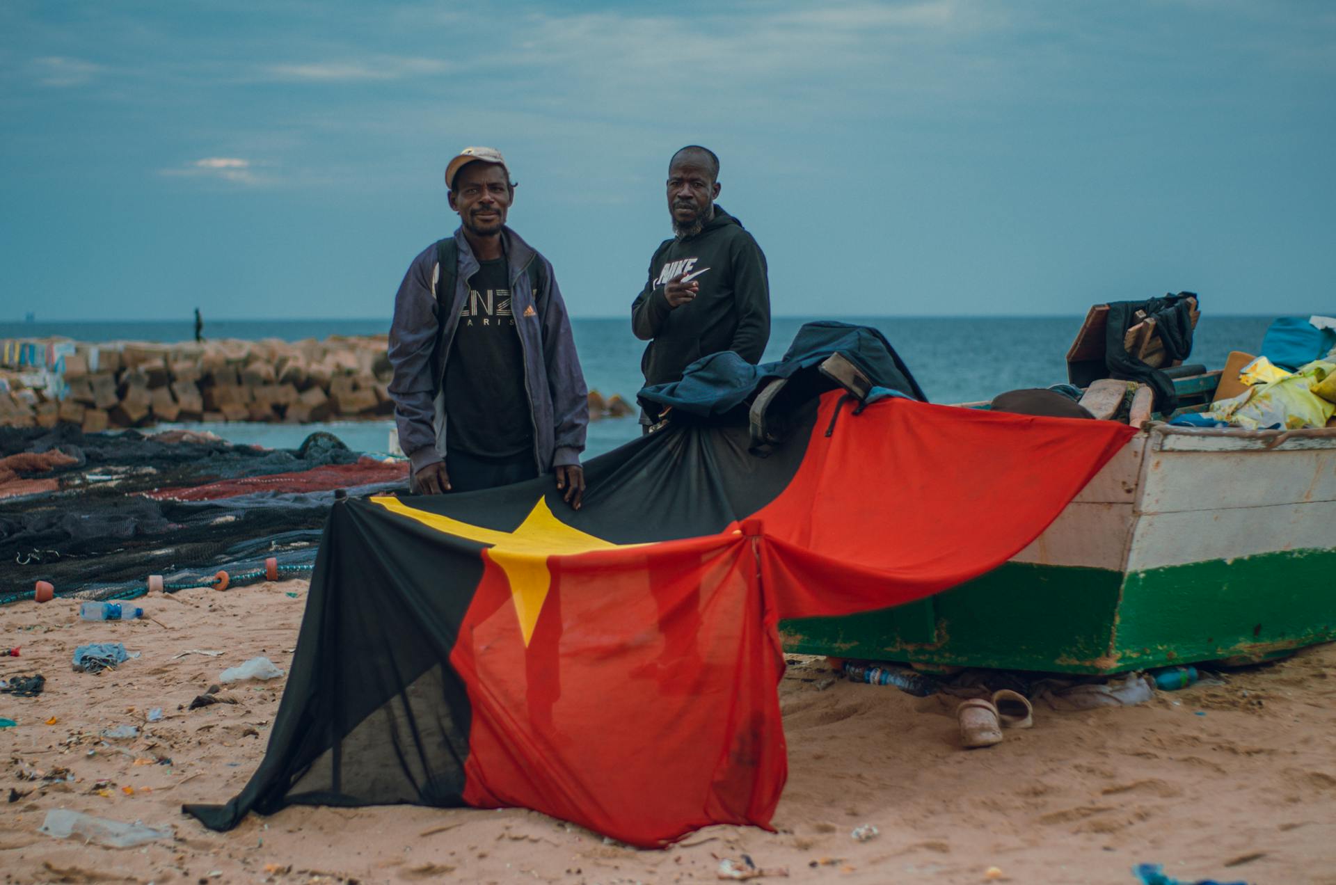 Two men by the sea with the Angolan flag, embodying friendship and culture.