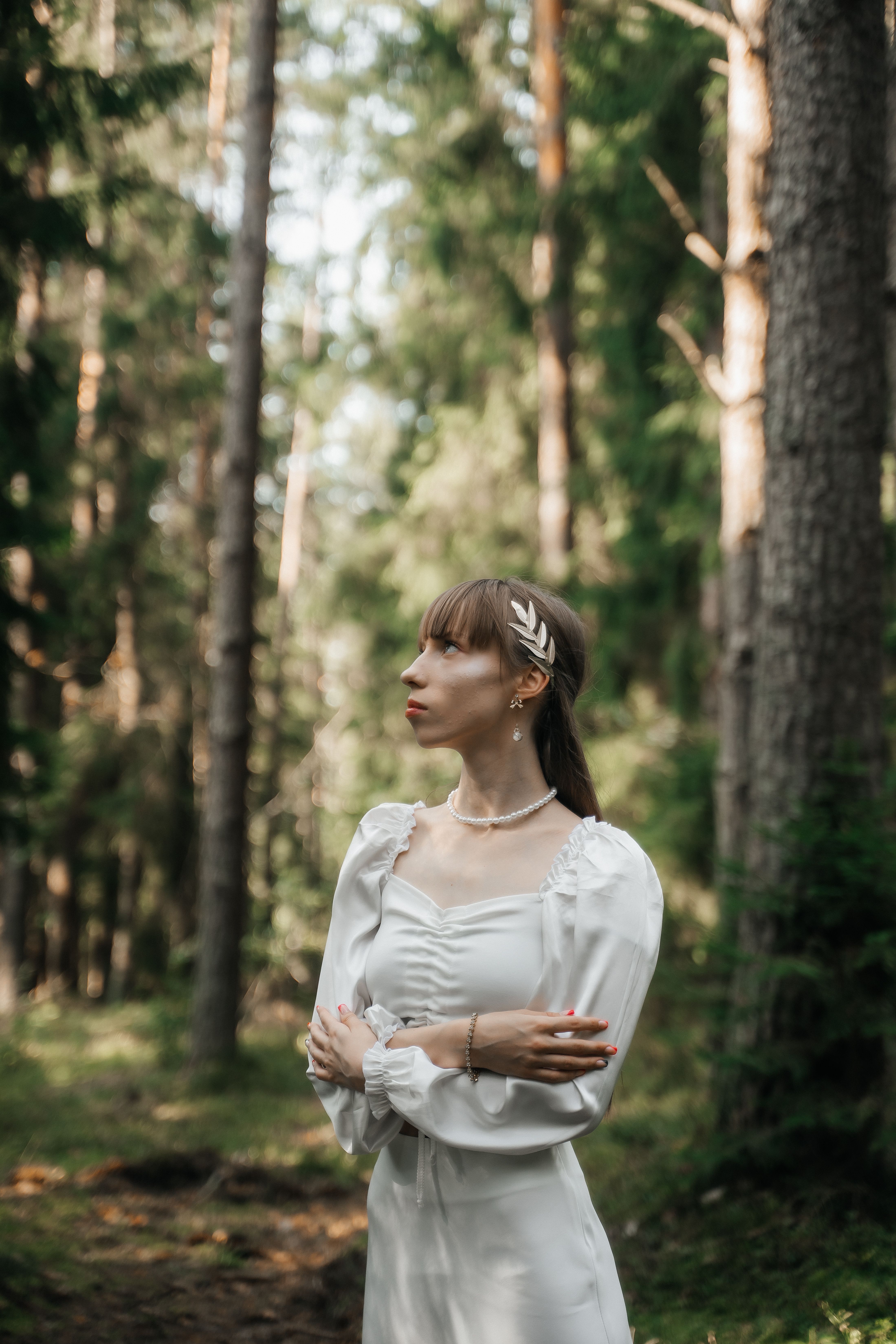 A woman in a white dress stands gracefully in a sunlit forest, embodying elegance and tranquility.