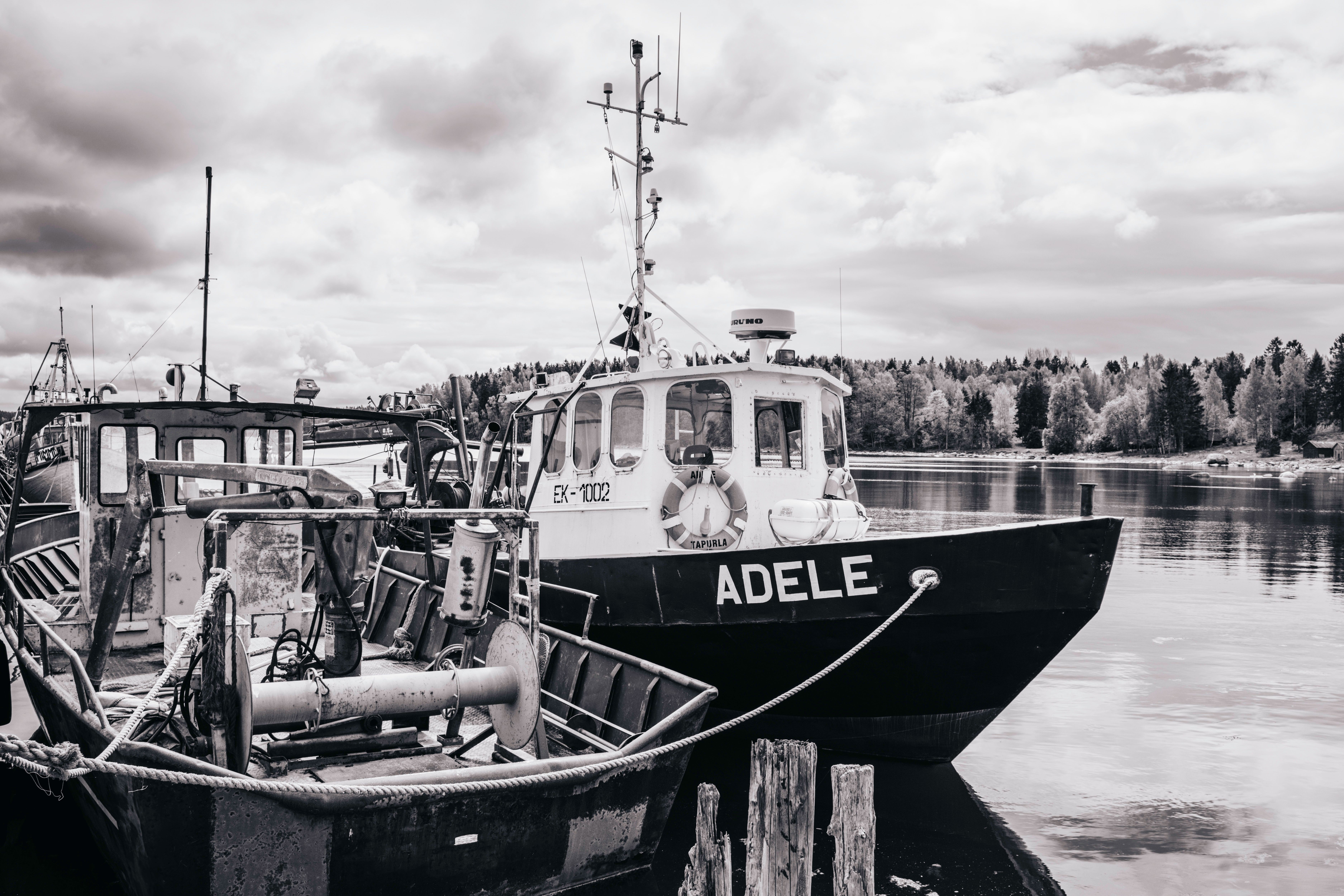 A serene scene of fishing boats docked by the shore with a calm reflective water body and cloudy sky.